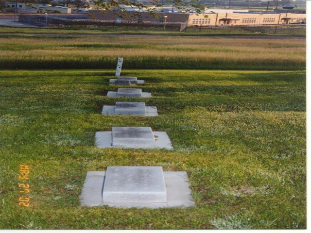 Veteran's headstones in a row with the Medium Security Unit in the distance.